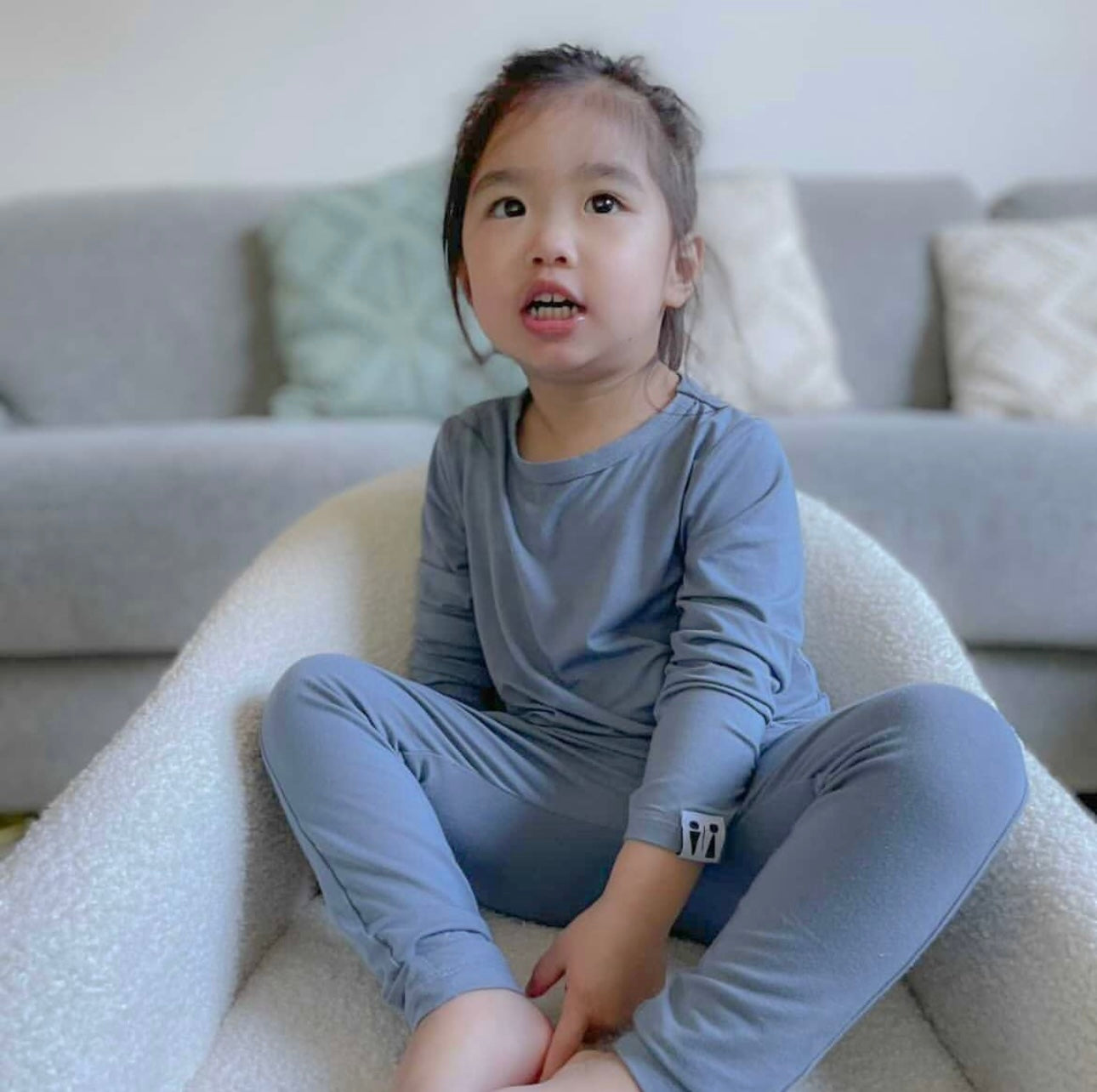 Child sitting on a bean bag chair wearing a blue Baby Todd & Co. bamboo outfit