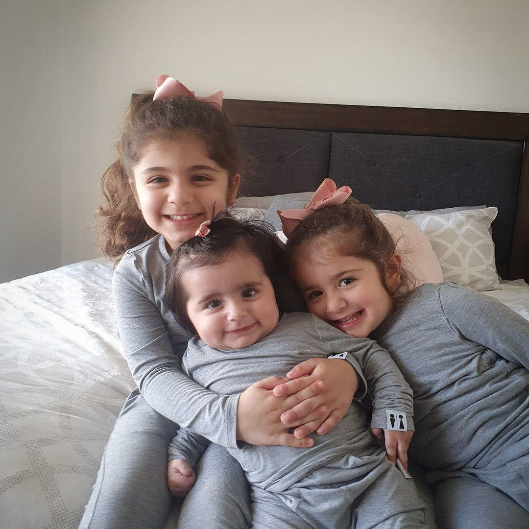 Three children in matching outfits sitting on a bed.